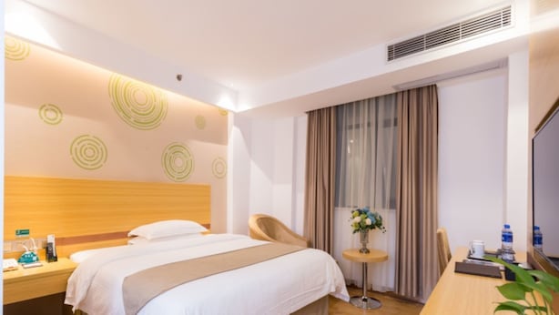 A hotel room with a bed, bedside table, chair, desk, and a small table with a vase of flowers.