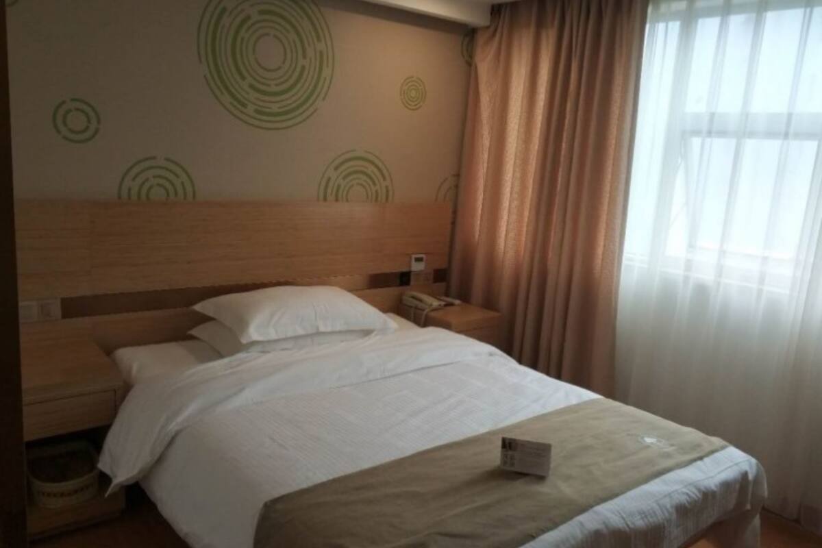 A hotel room with a wooden headboard, a bed with white linens, a bedside table with a phone, and a window with curtains.