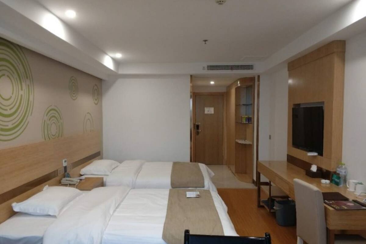 A hotel room with two beds, a desk with a chair, a television, and a bathroom visible through an open door.