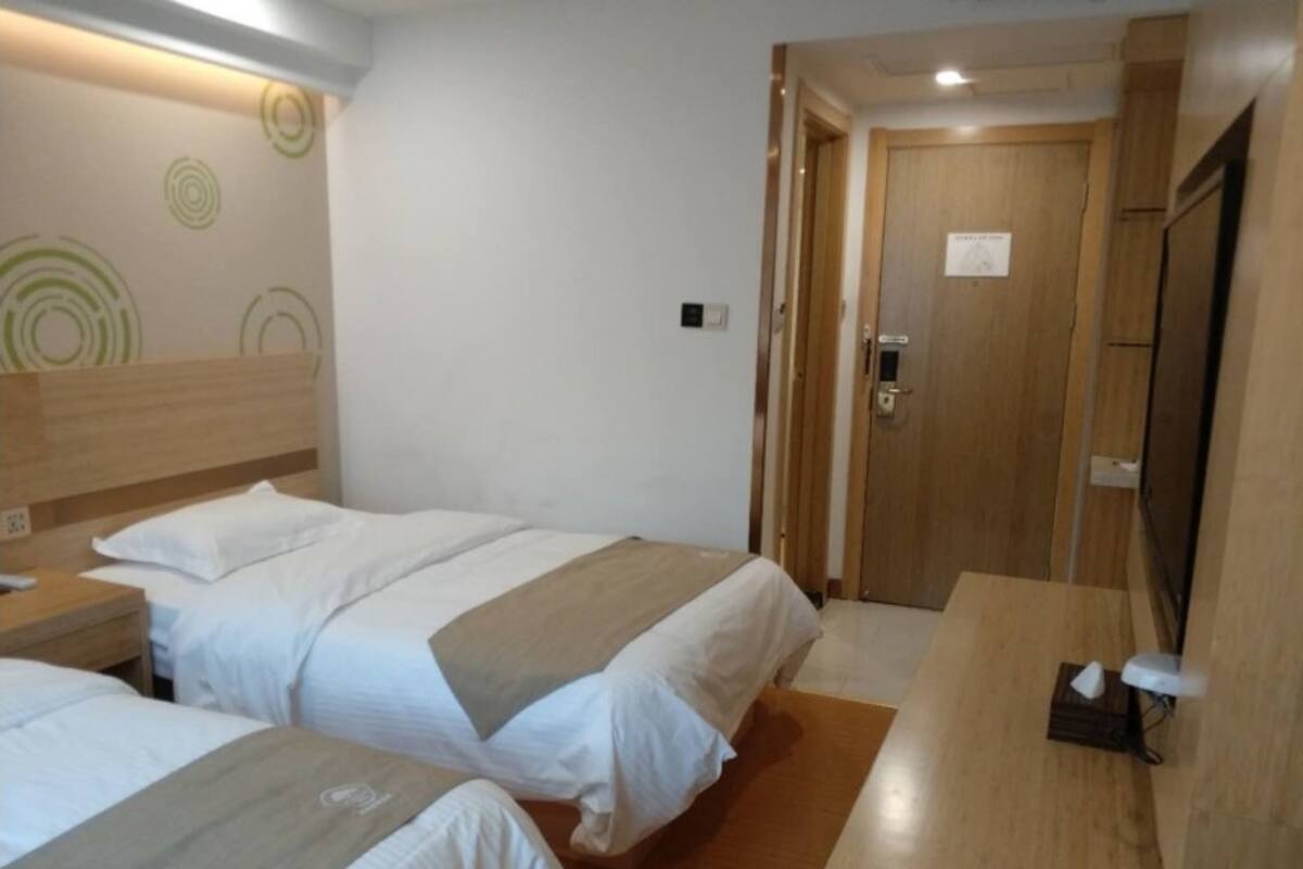 A hotel room with two beds, a wooden headboard, a bedside table, a desk, and a television.
