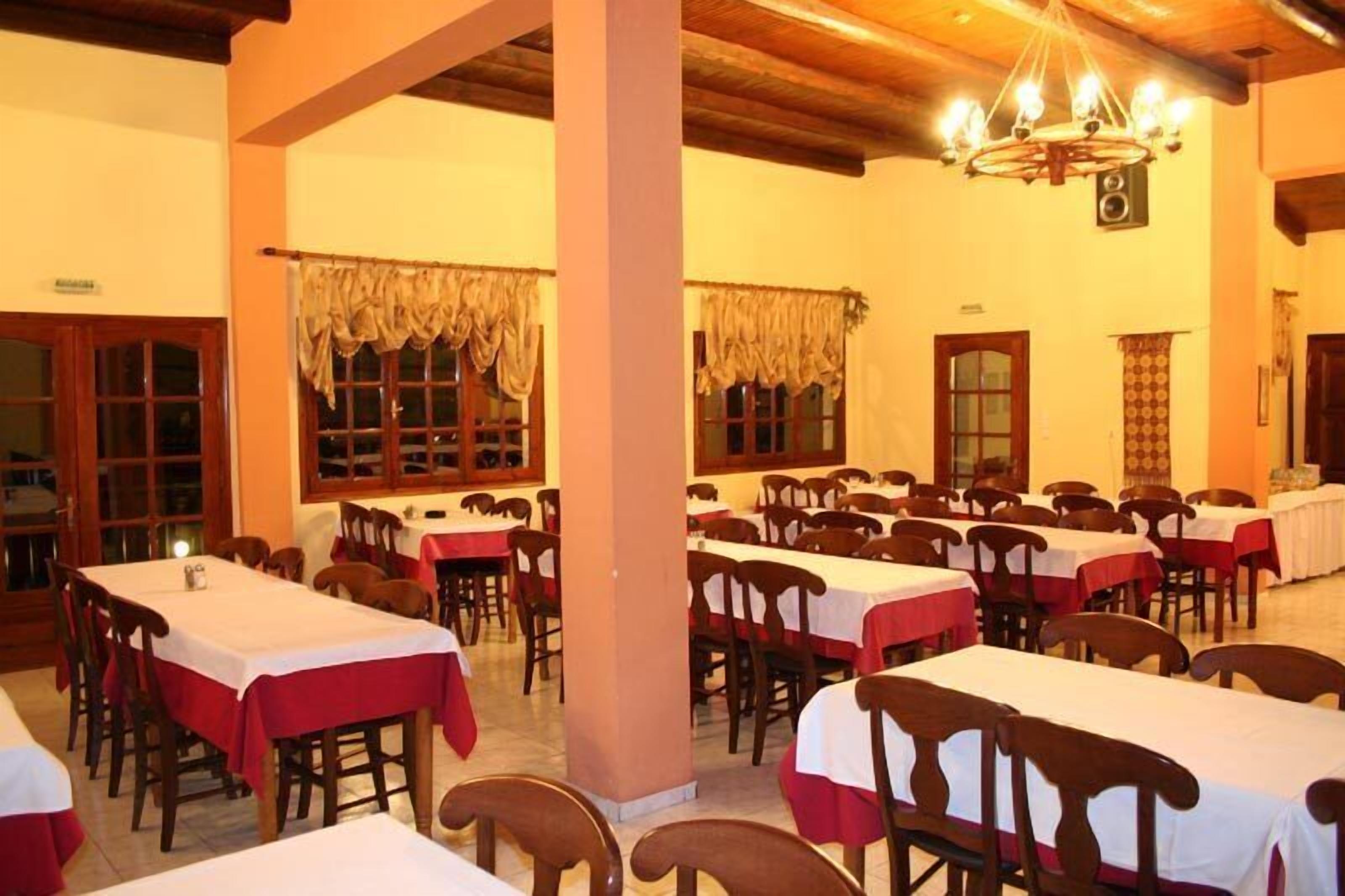 Une salle à manger avec de nombreuses tables et chaises, des poutres en bois au plafond et un lustre.