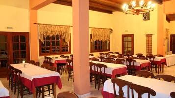 Une salle à manger avec de nombreuses tables et chaises, des poutres en bois au plafond et un lustre.