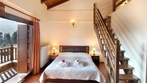 Une chambre avec un grand lit, deux lampes de chevet, un escalier en bois et un balcon avec vue.