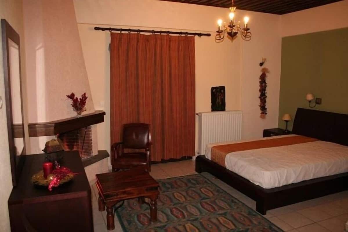 A bedroom with a bed, a chair, a table, a fireplace, and a curtain.