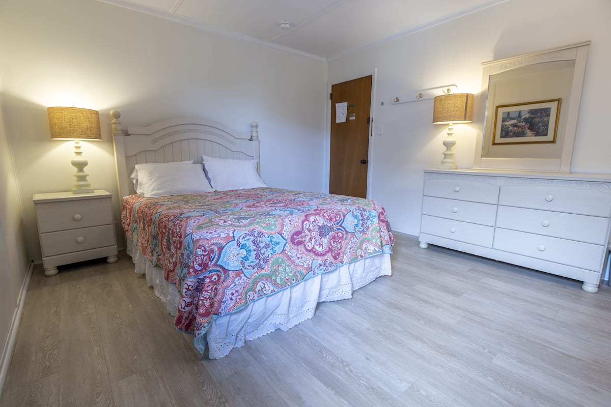 Une chambre à coucher avec un lit, des tables de chevet, une commode et une porte.