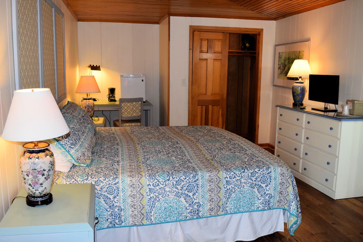Une chambre à coucher avec un lit, une commode, une lampe, un téléviseur et une porte.