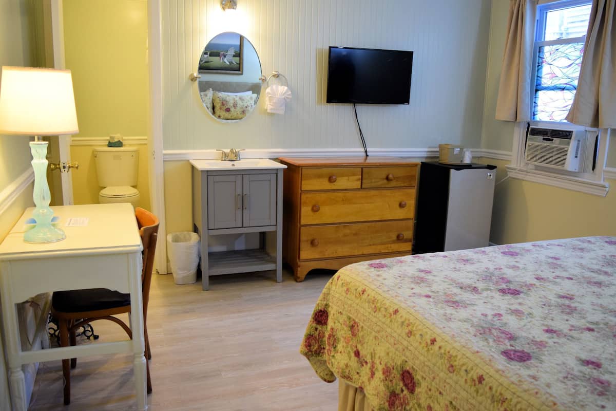 Une chambre comprenant un lit, un bureau avec une lampe, une commode, un miroir, des toilettes et un téléviseur.