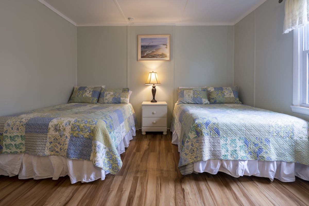 Une chambre avec deux lits, une table de chevet avec une lampe et un tableau au mur.