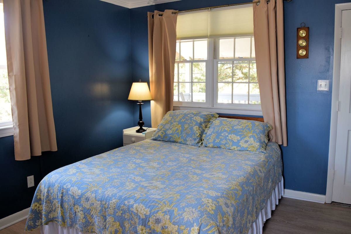 Une chambre à coucher avec un lit, une table de chevet, une lampe et une fenêtre avec des rideaux.