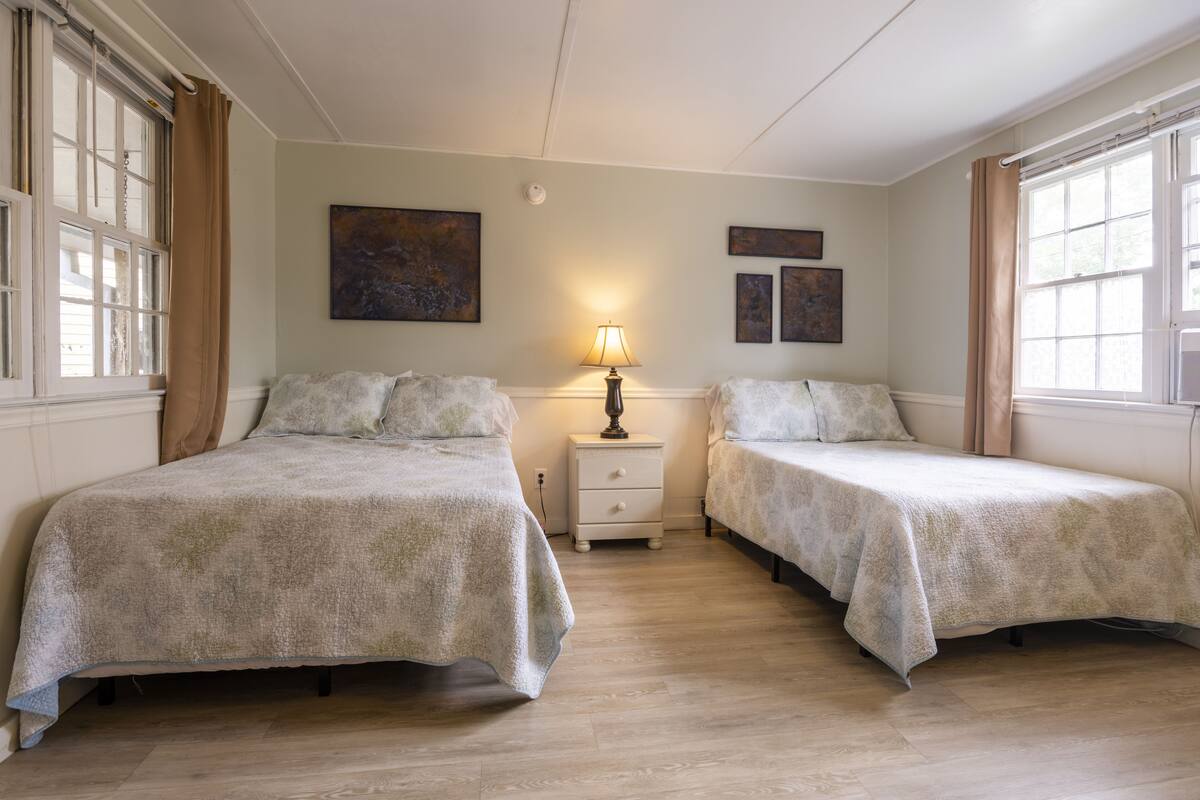 Une chambre avec deux lits, une table de chevet avec une lampe et des œuvres d’art accrochées aux murs.