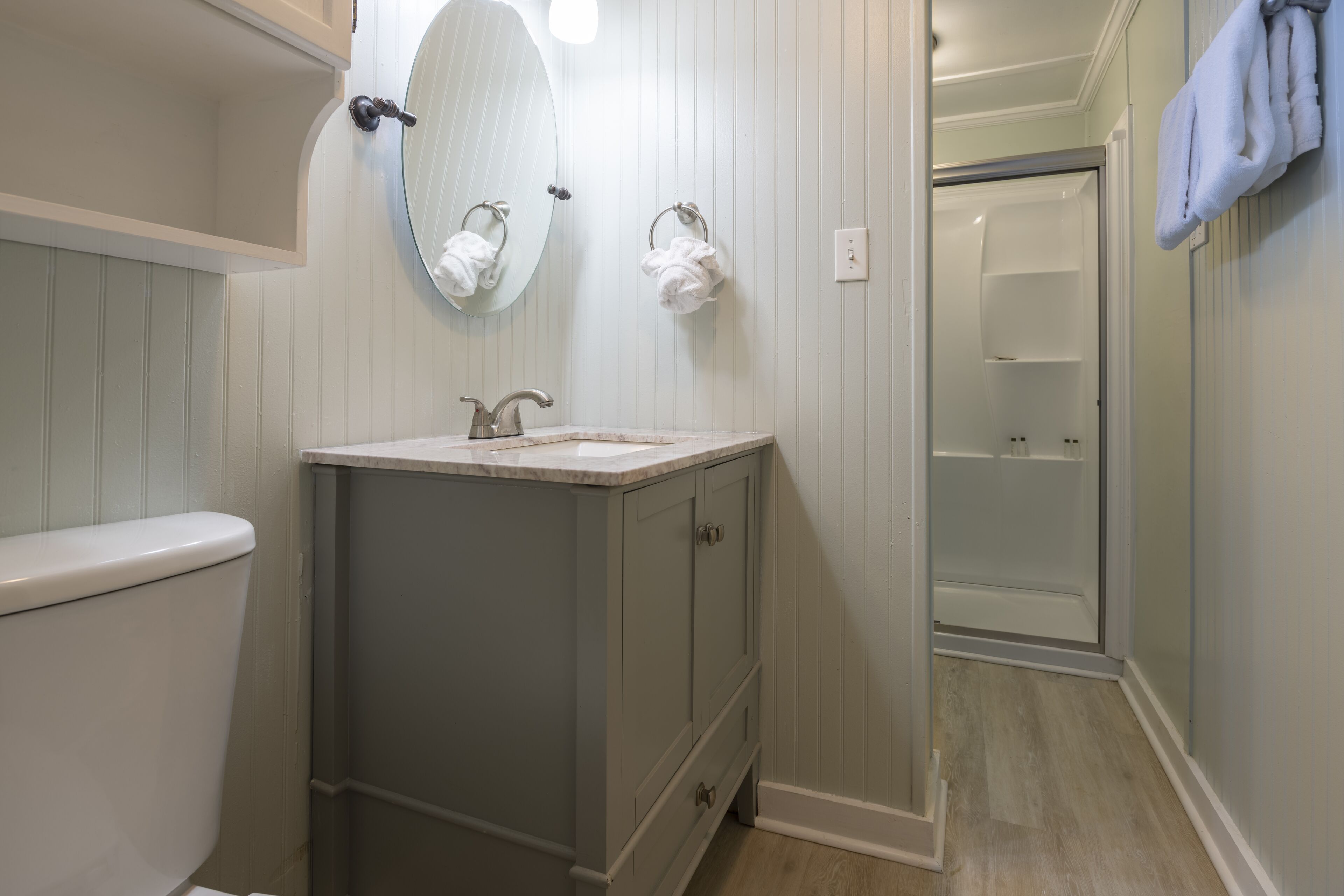 A bathroom with a toilet, sink, mirror, and shower.