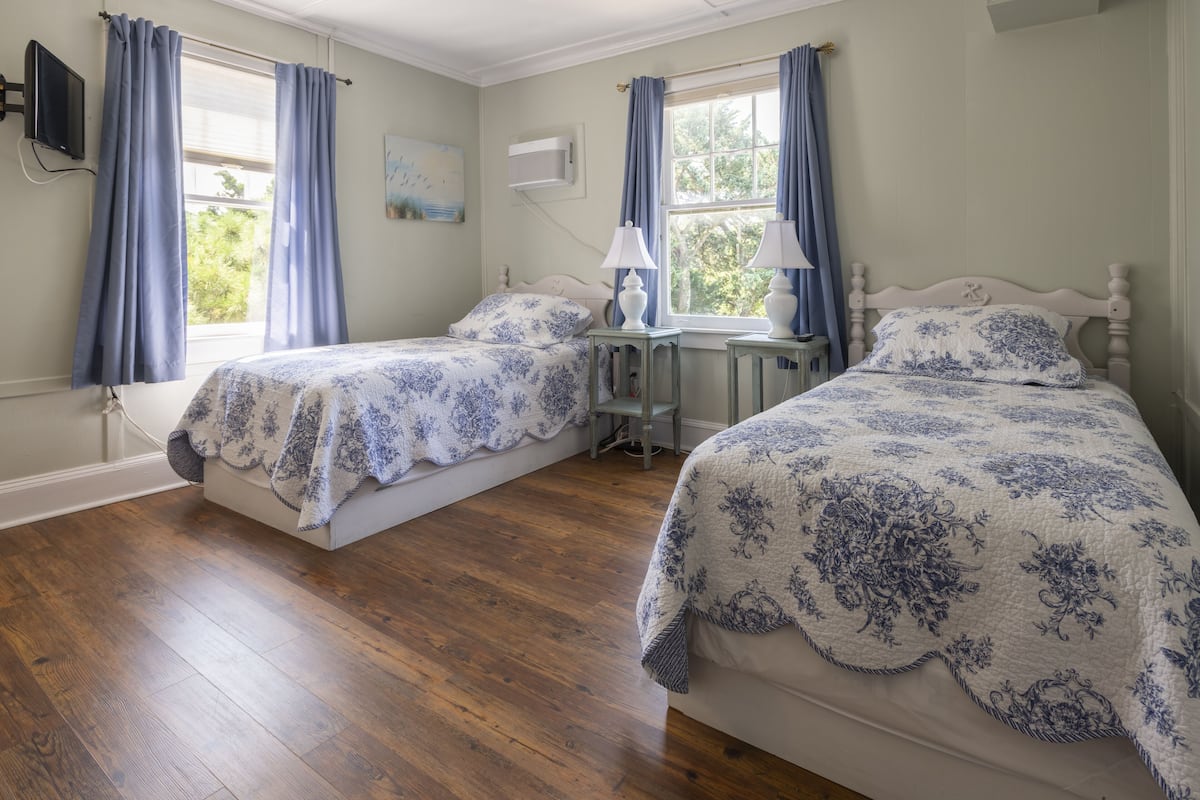 Une chambre avec deux lits, un plancher en bois et une fenêtre avec des rideaux.