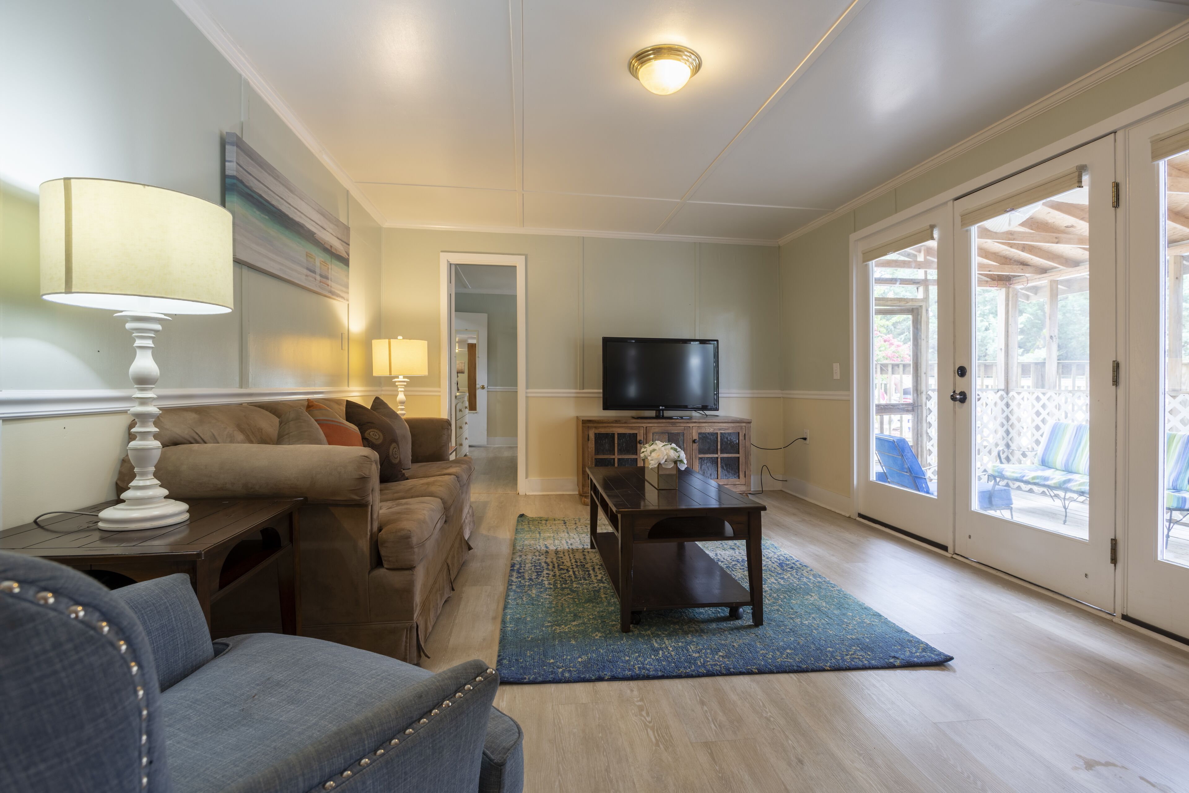 A living room with a sofa, a coffee table, a TV, and a view of the outside through a glass door.