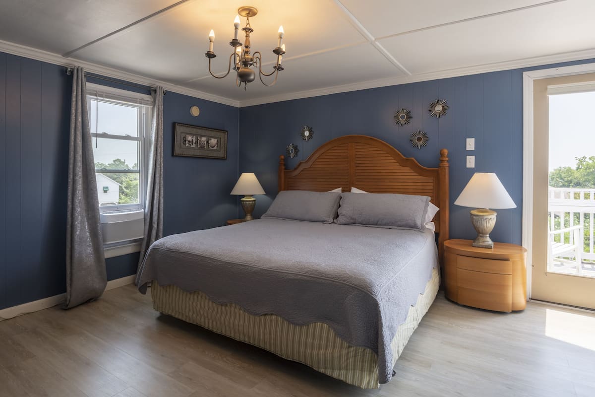 Une chambre à coucher avec un grand lit, deux tables de chevet avec des lampes, un lustre, une fenêtre avec des rideaux et des éléments de décoration murale.