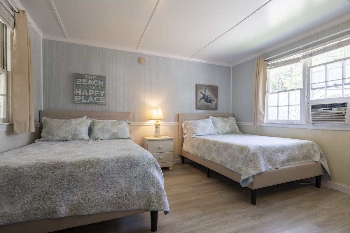 Une chambre avec deux lits, une table de chevet avec une lampe, une horloge murale et un panneau décoratif sur le thème de la plage.