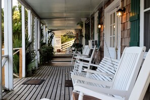 A wooden porch with white chairs and a wooden staircase leading to a door. - Blackbeard's Lodge (Ocracoke)