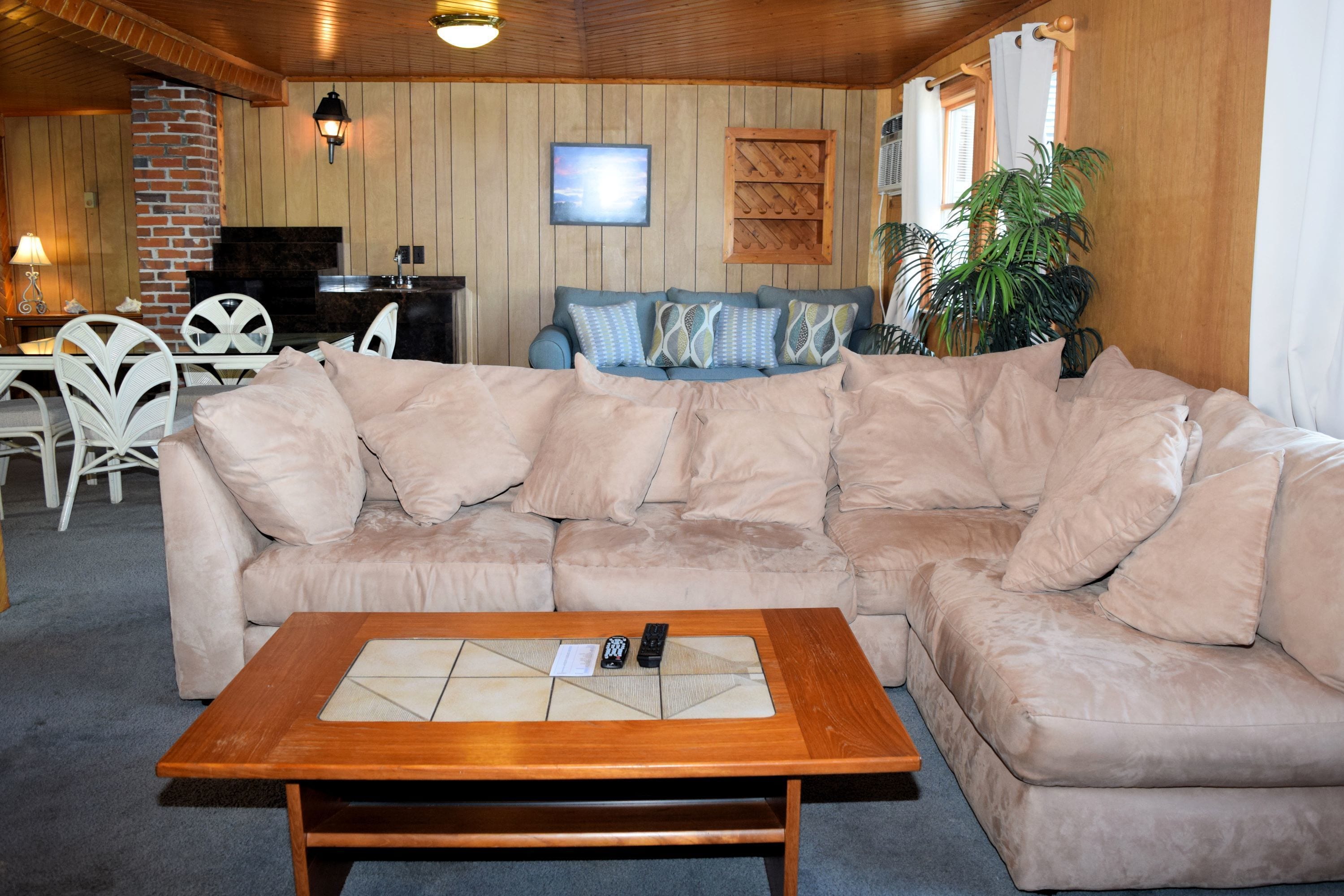 Una sala de estar acogedora con un sofá seccional color beige, una mesa de centro de madera y un televisor montado en la pared.
