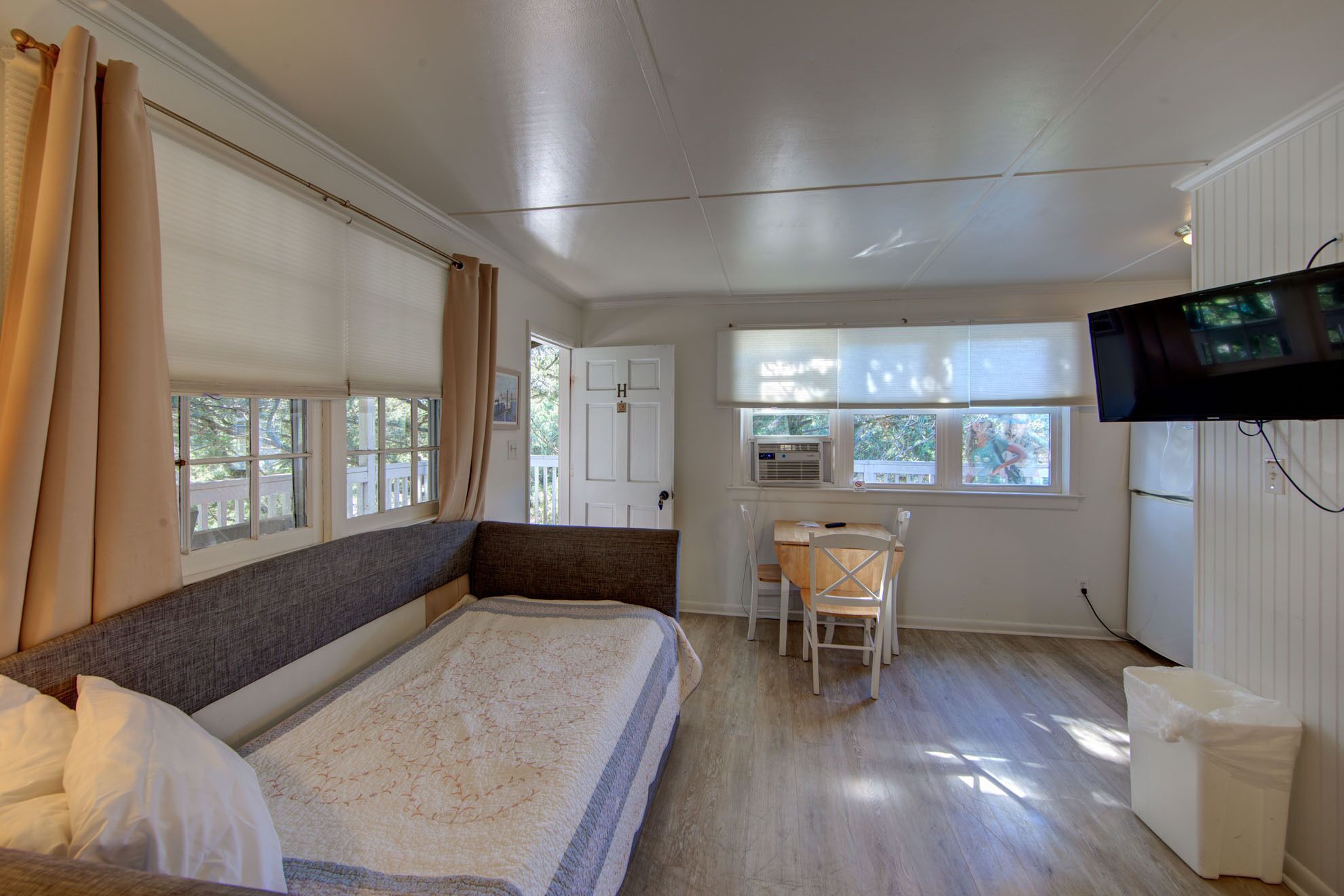 A room with a bed, a desk, a chair, a television, and windows with blinds.