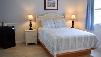 A neatly made bed with a patterned bedspread, two bedside lamps, a small bedside table with a lamp, and a framed picture on the wall.
