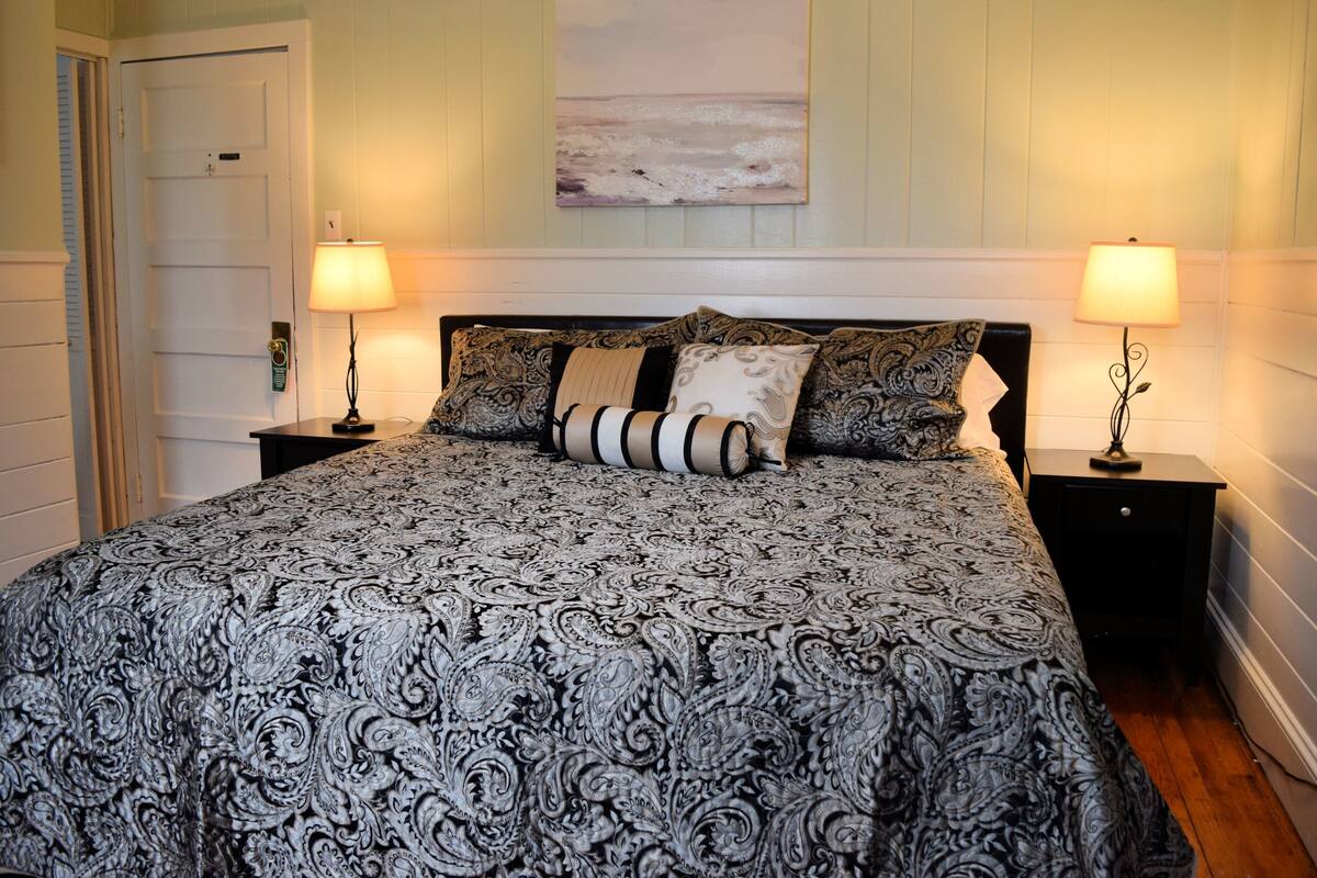 Une chambre à coucher avec un grand lit, deux tables de chevet avec des lampes, une porte et une œuvre d’art accrochée au mur.