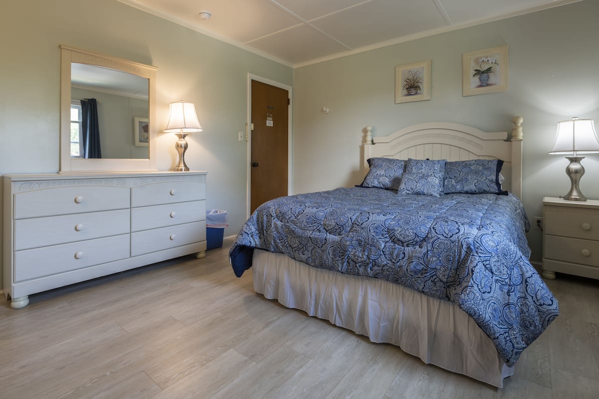 Une chambre à coucher comprenant un lit, une commode, une table de chevet et un miroir.