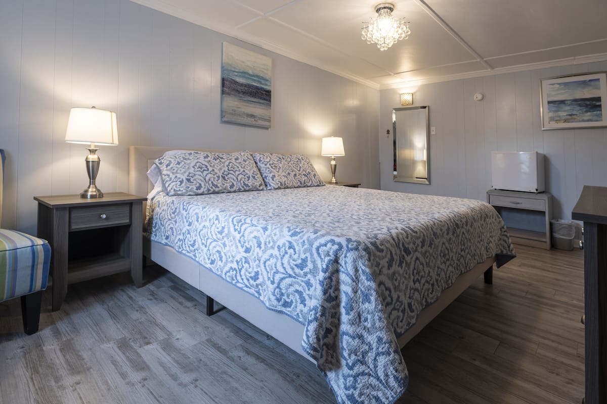 Une chambre à coucher avec un lit, deux tables de chevet avec des lampes, une chaise, un téléviseur et un tableau au mur.