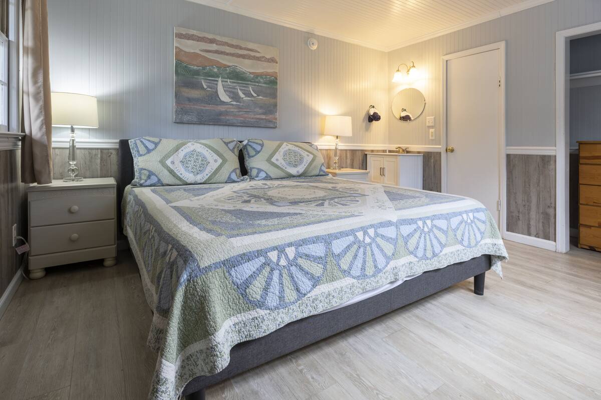 Une chambre à coucher avec un grand lit, une table de chevet, une commode, un miroir et une porte donnant sur un placard.