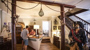 Un interior de madera con una barra central que dice 'Aventura', una escalera con una estatua de pirata y decoración náutica.