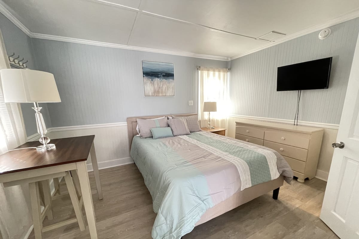 Une chambre à coucher comprenant un lit, des tables de chevet, un bureau, un téléviseur à écran plat et une fenêtre avec des rideaux.