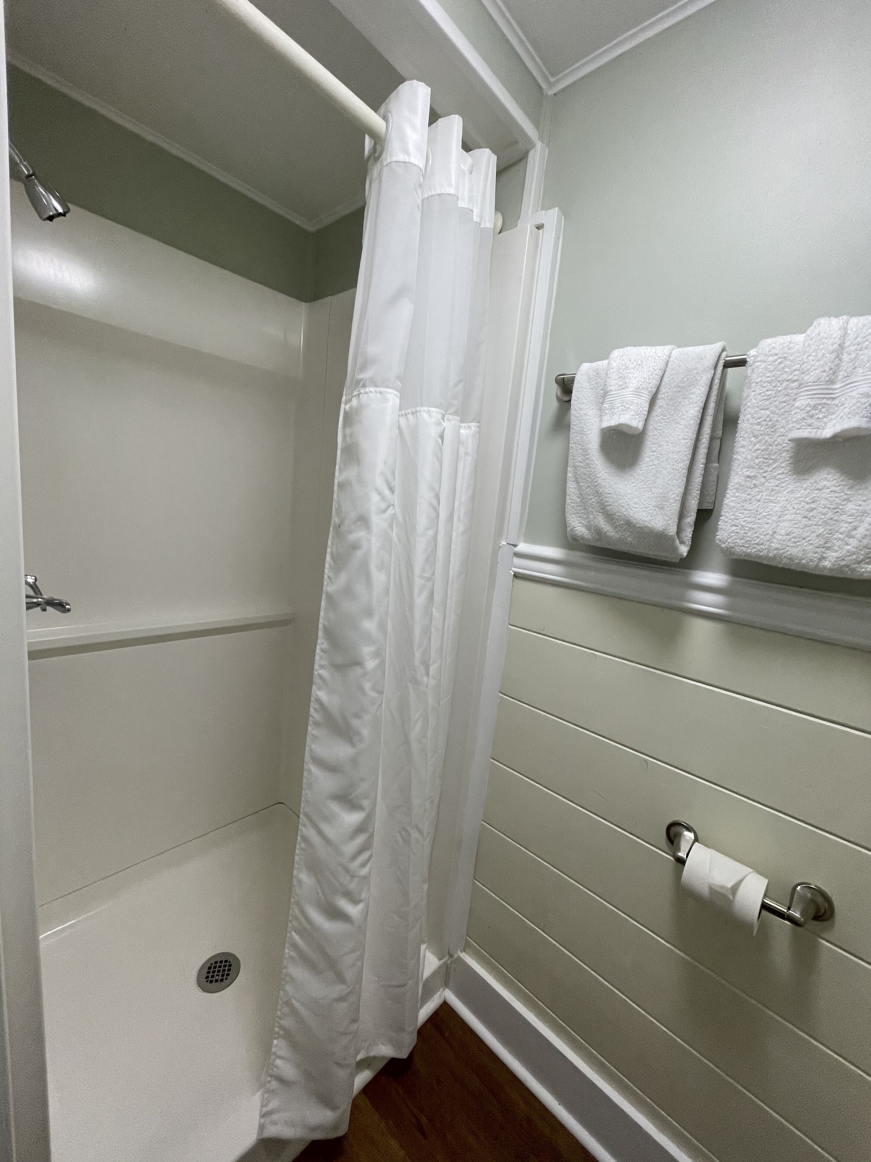 Un baño con cortina de ducha, toallero con toallas y dispensador de papel higiénico.