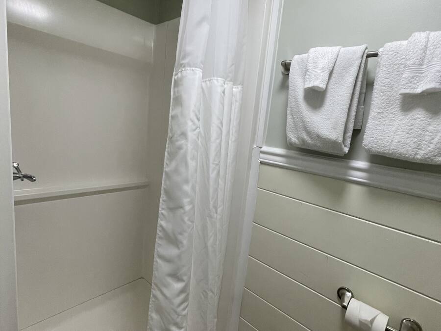 Un baño con cortina de ducha, toallero con toallas y dispensador de papel higiénico.