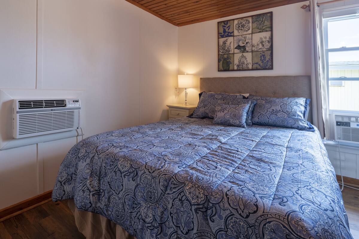 Une chambre à coucher avec une couvre-lit à motifs, une lampe de chevet, un climatiseur et un élément décoratif mural.