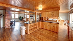 Una cocina amplia con armarios de madera y una isla central, un comedor con pared de ladrillo decorativa y un gran ventanal que proporciona luz natural.