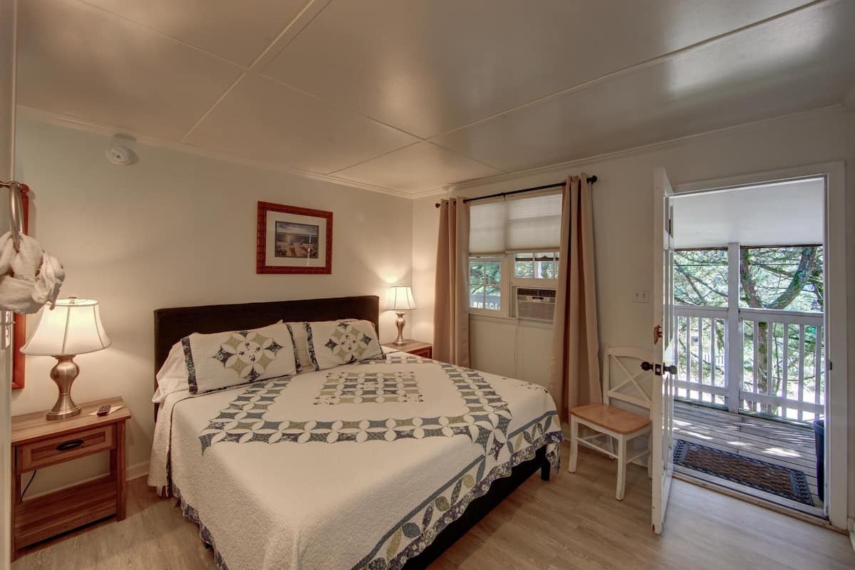 Une chambre à coucher avec un lit, des lampes de chevet, un tableau au mur, une fenêtre avec des rideaux et une chaise près de la porte.
