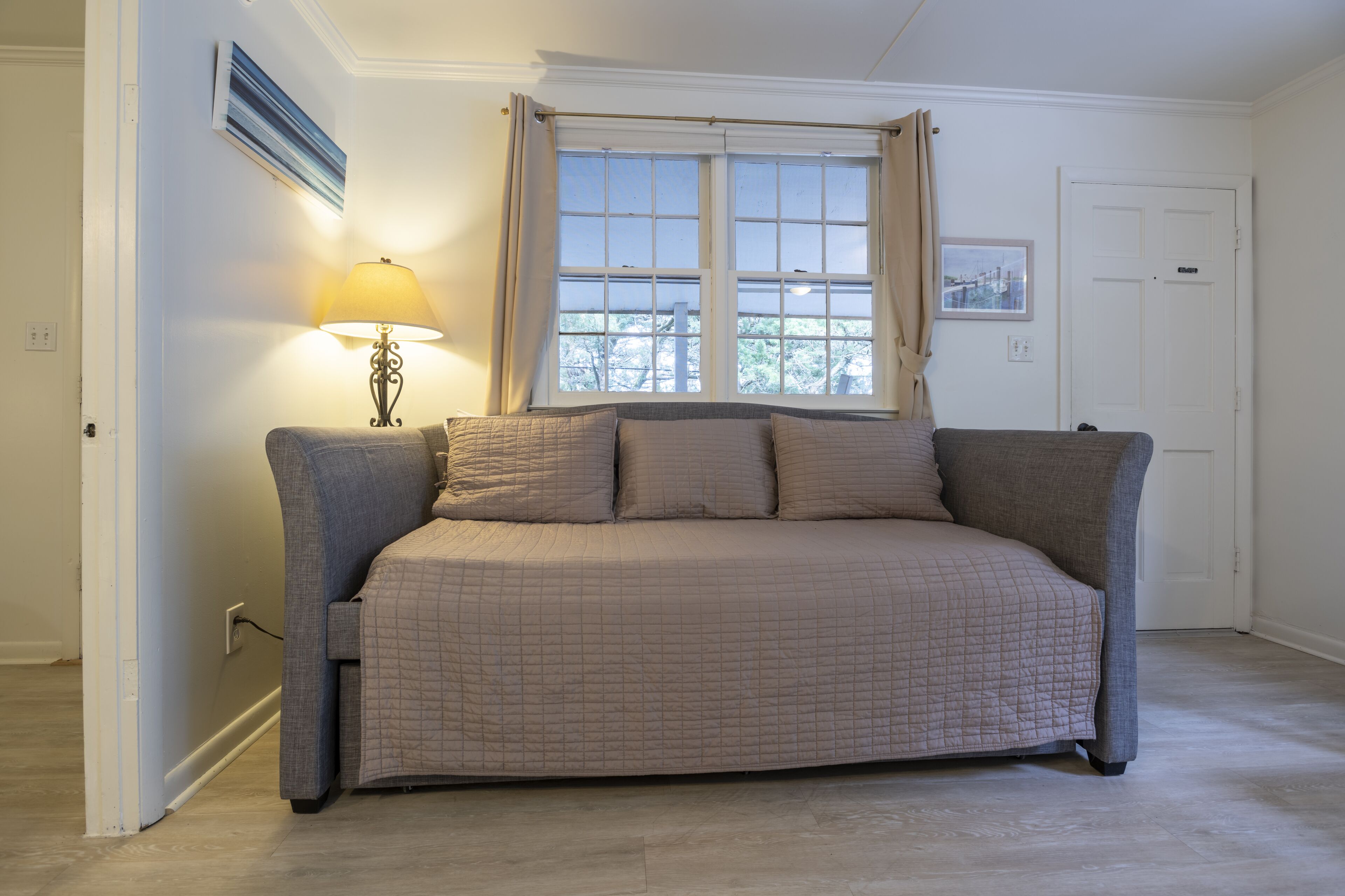 A bedroom with a bed, a window with curtains, a lamp, and a door.