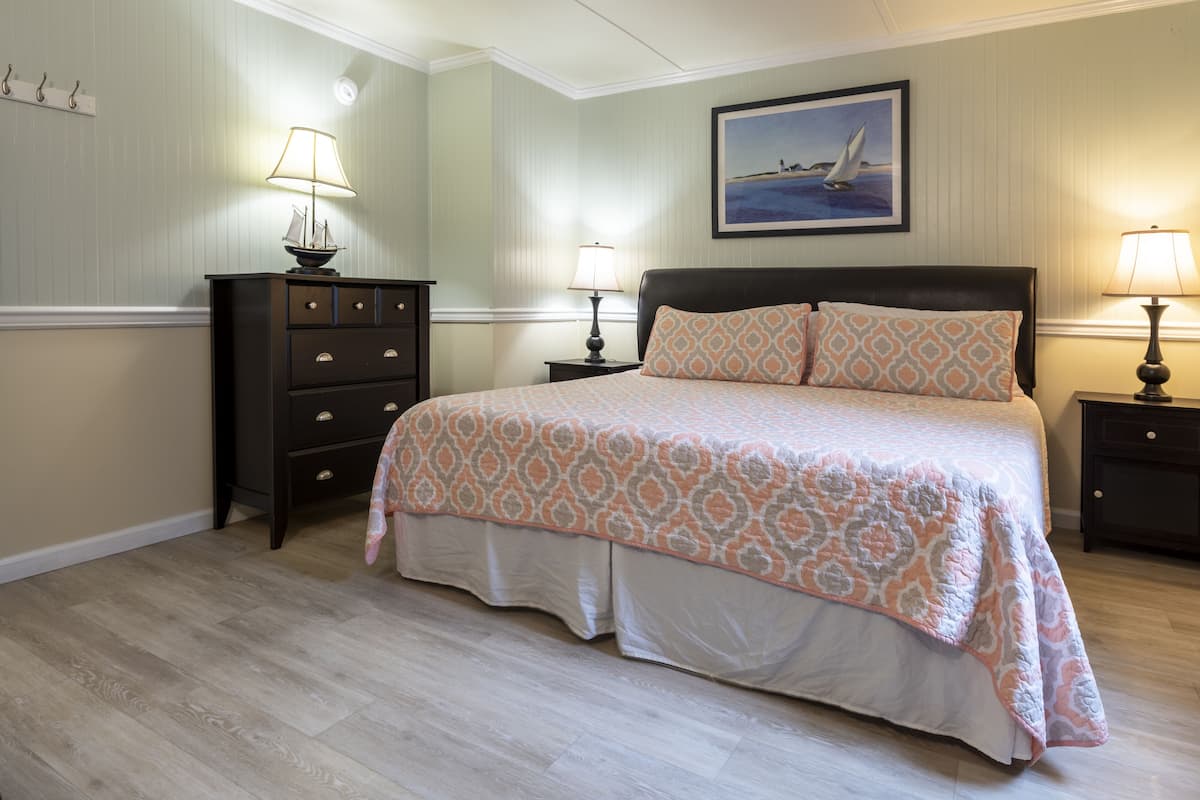 Une chambre à coucher bien rangée, avec un lit, deux tables de chevet, une commode et un tableau au mur.