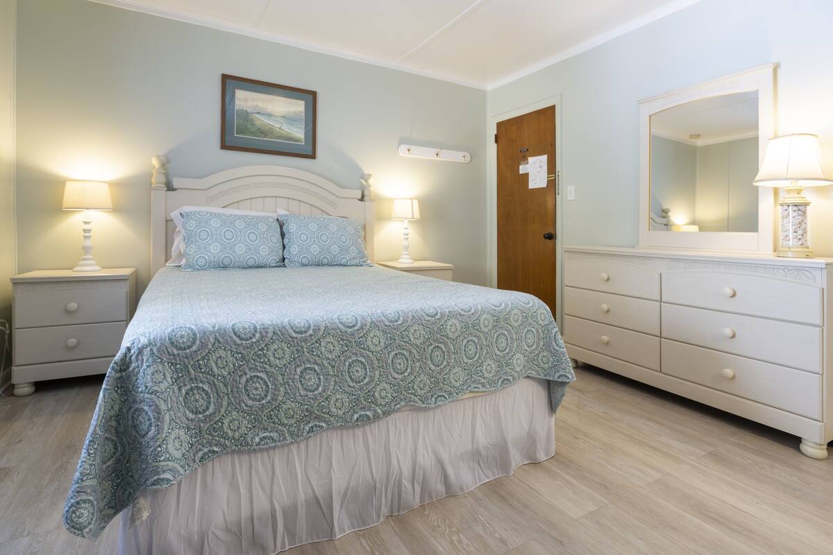Une chambre à coucher avec un lit, deux tables de chevet avec des lampes, une commode et un miroir.