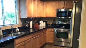A modern kitchen with wooden cabinets, stainless steel appliances, and a black countertop.