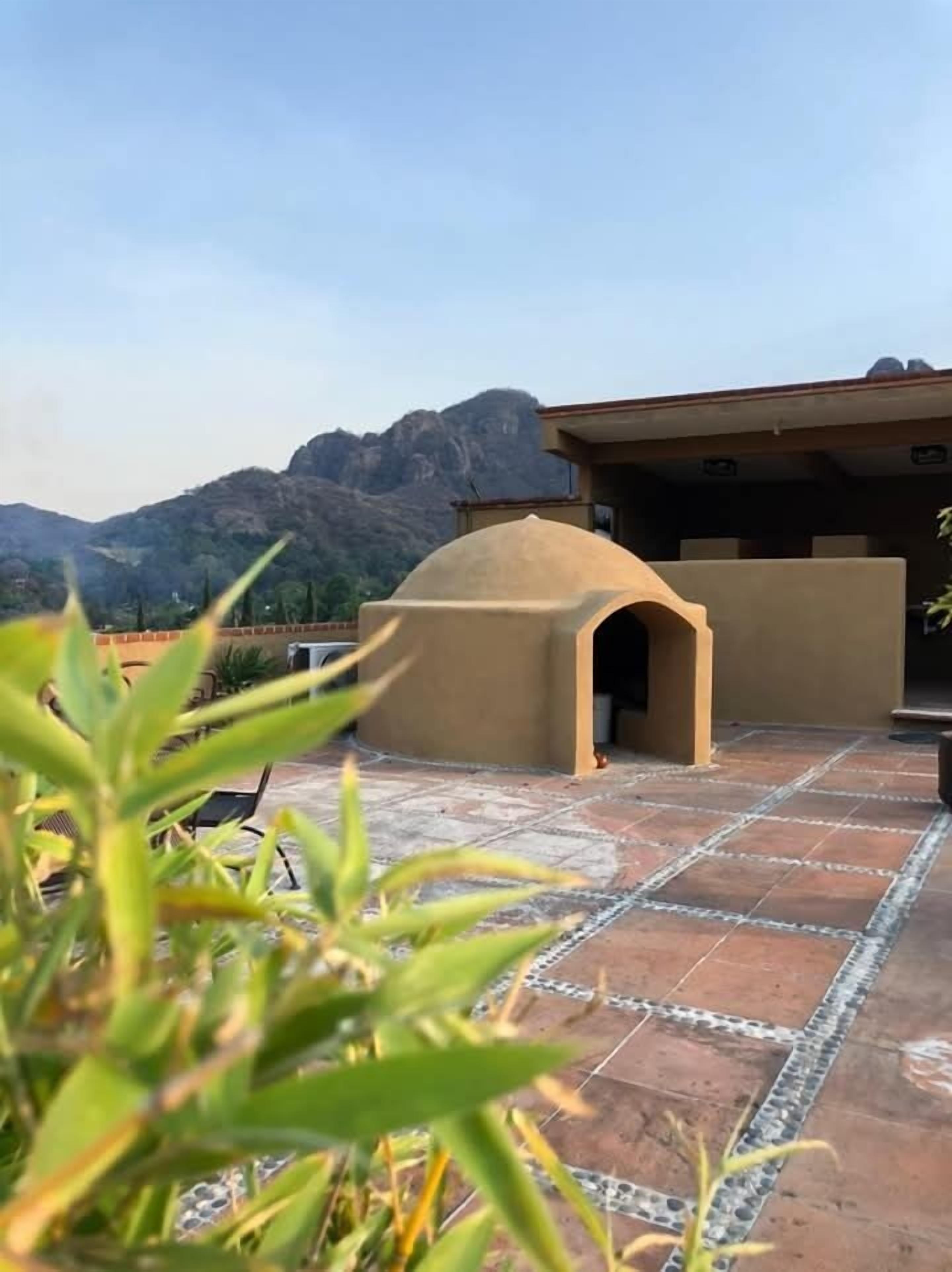 A patio area with a stone floor, a small covered structure, and a mountainous backdrop.