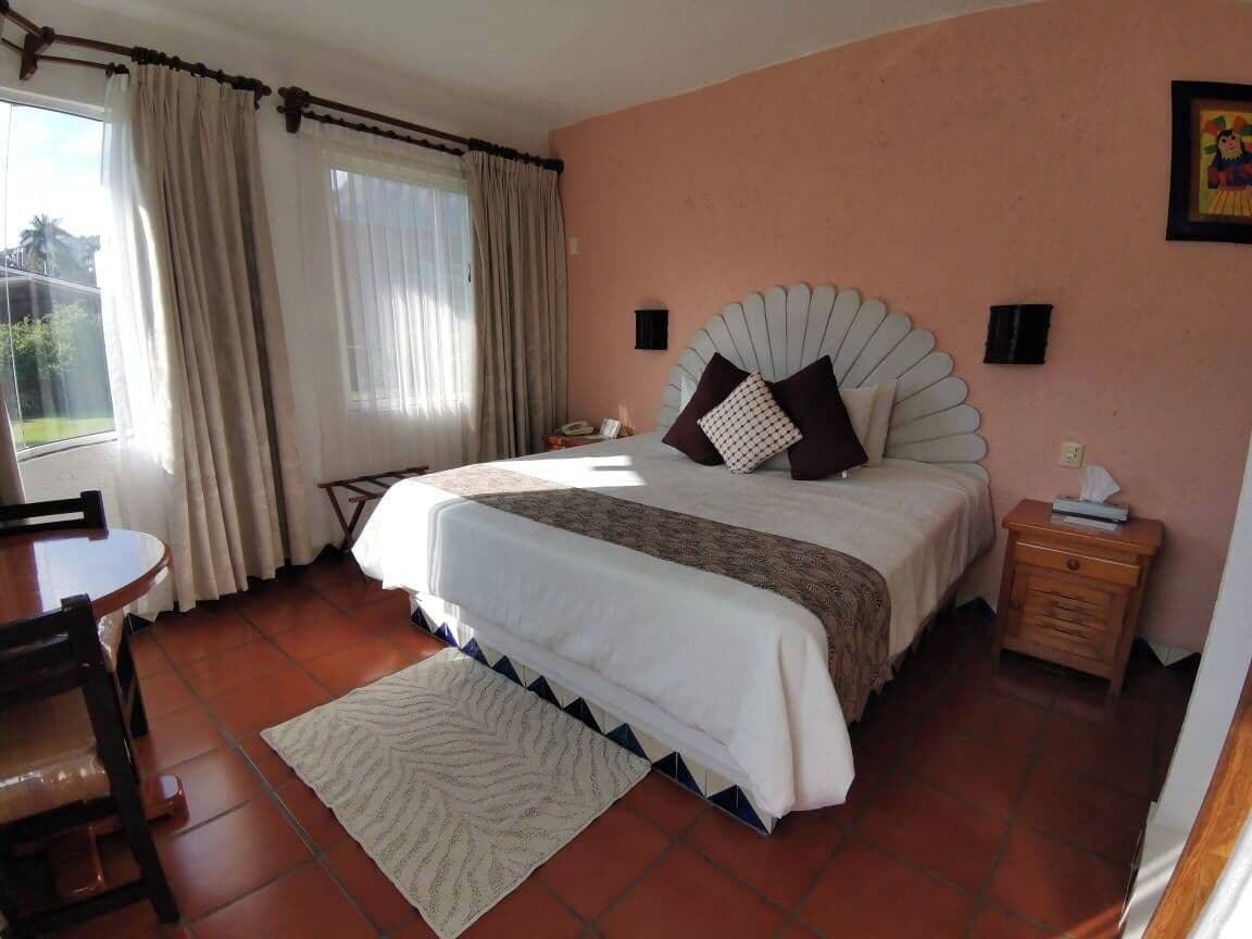 A bedroom with a bed, a bedside table, a chair, a desk, and a window with curtains.