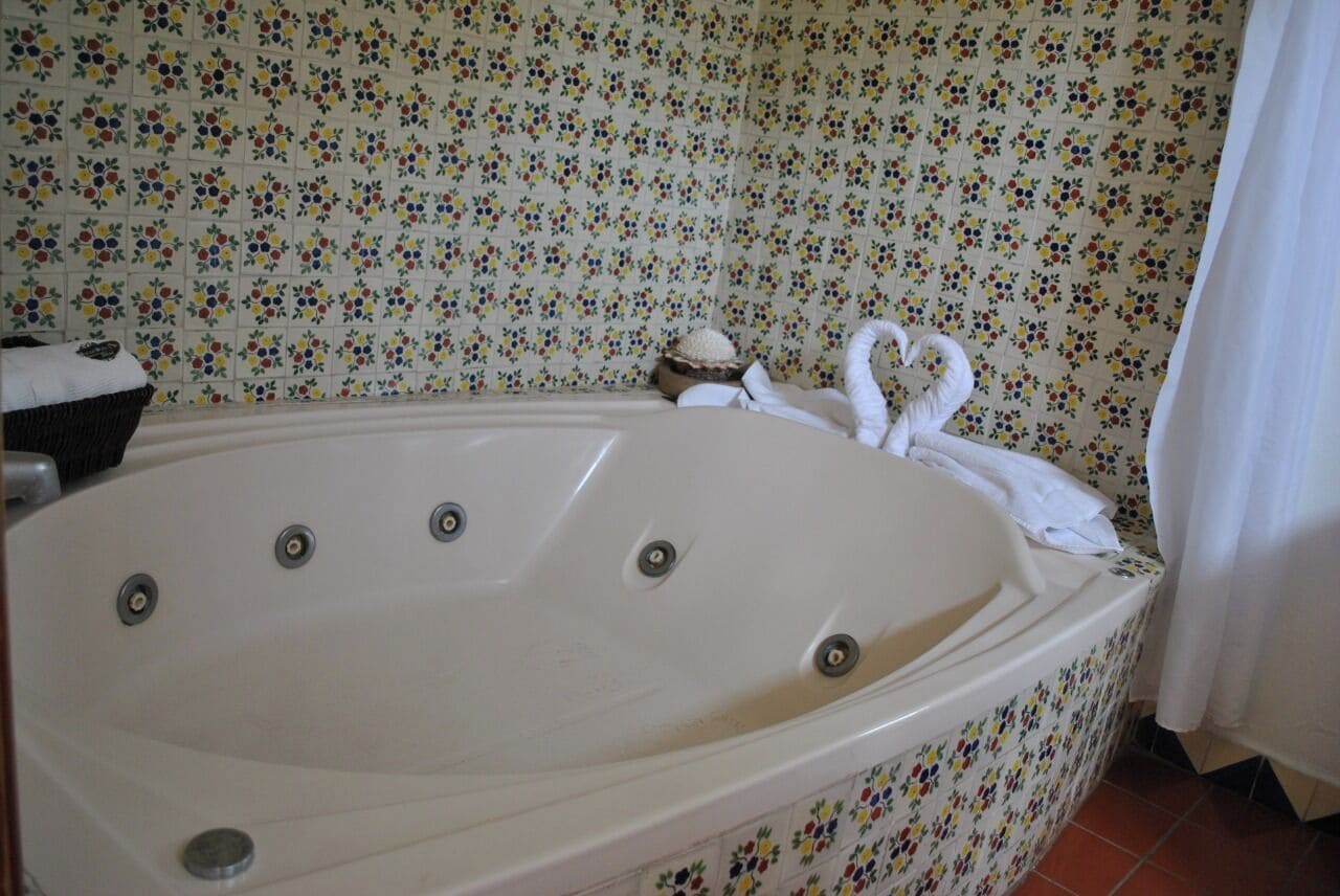 A large, white bathtub with four faucets, set against a floral-patterned wall.