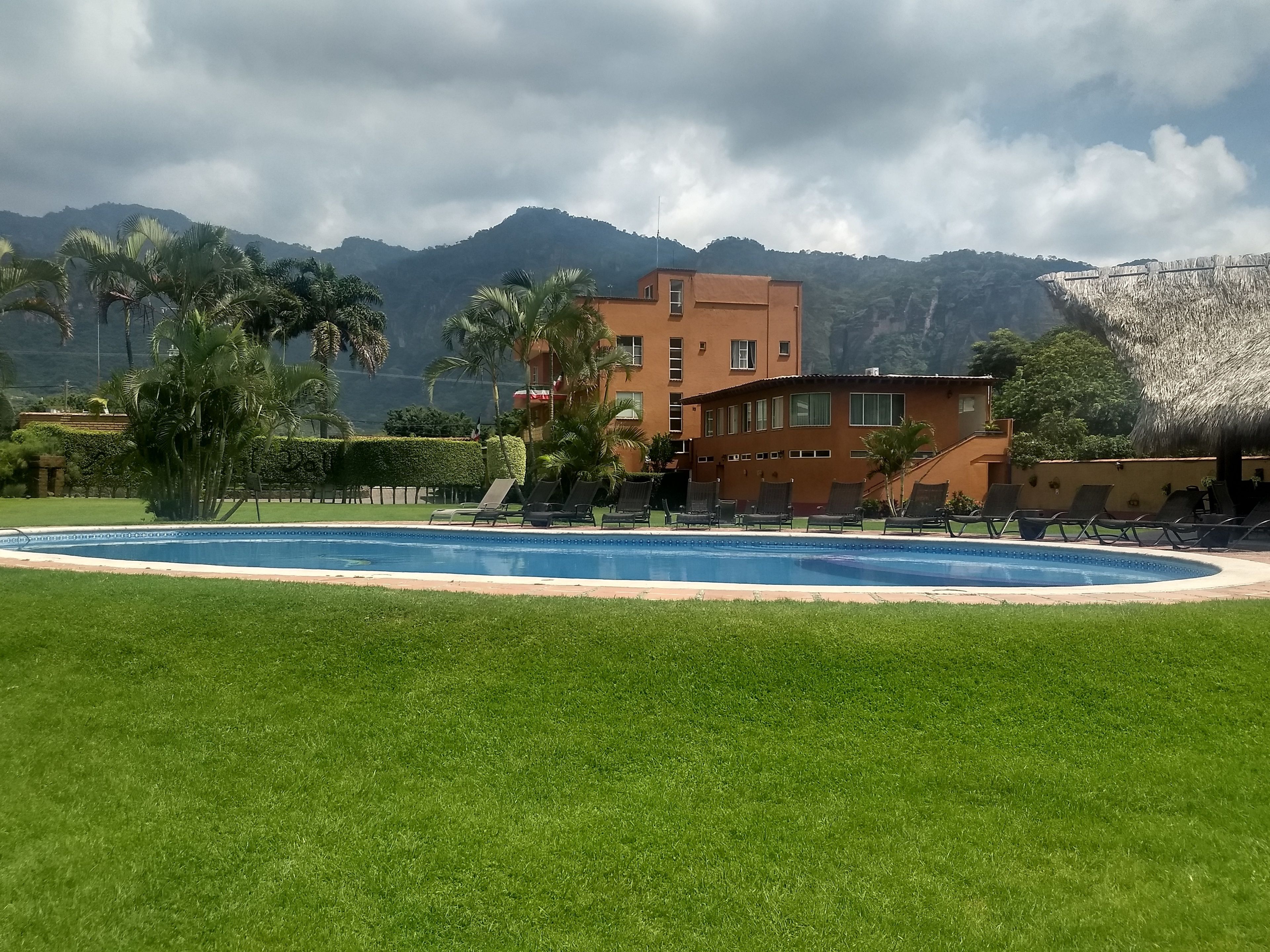 A pool area with lounge chairs, a building with multiple windows, and a mountainous backdrop.