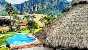 A resort with a swimming pool, a thatched-roof structure, and lush greenery. - Hotel Real del Valle Tepoztlan (Tepoztlán)