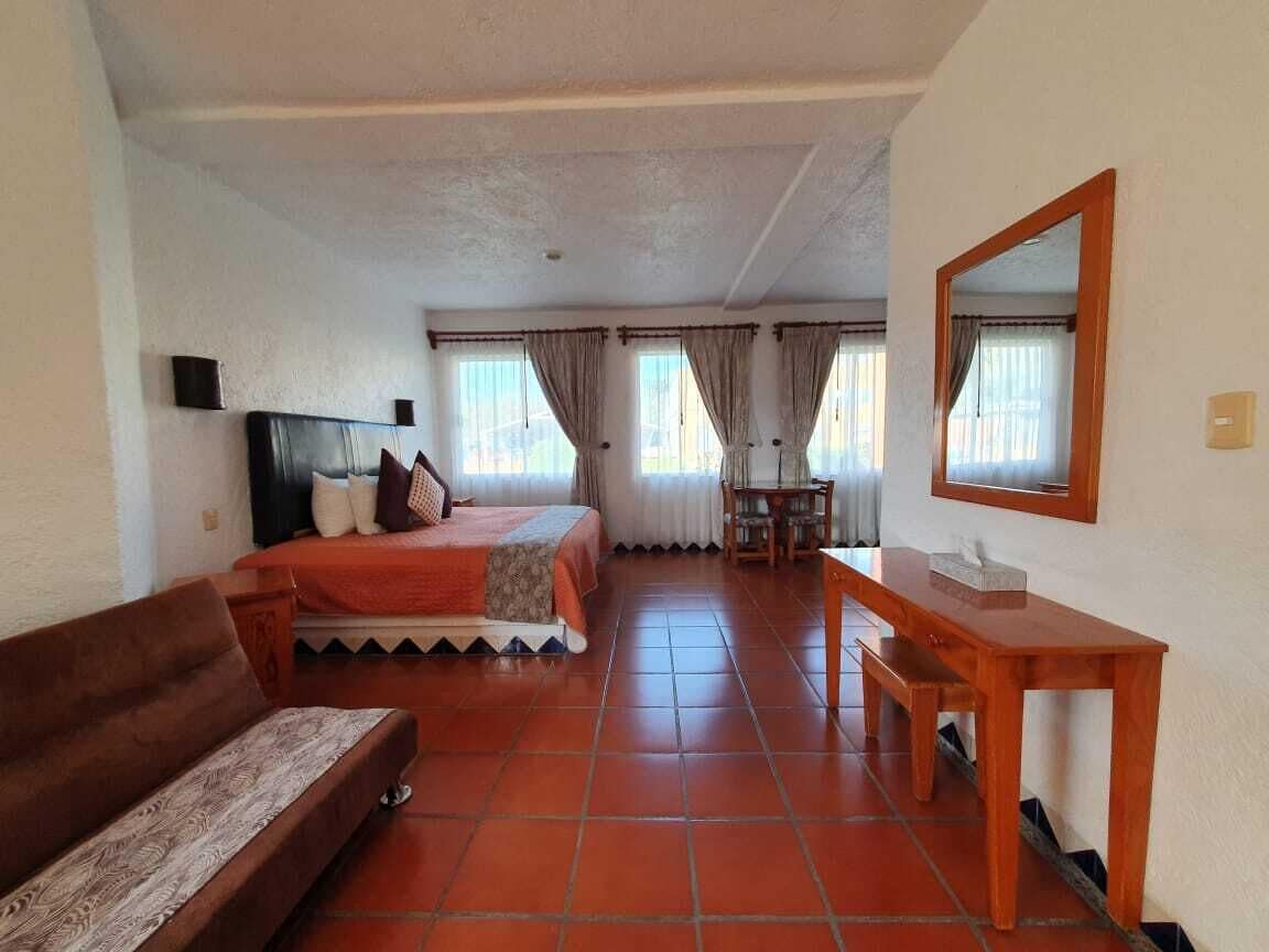 A hotel room with a bed, a wooden desk, a sofa, and a mirror.