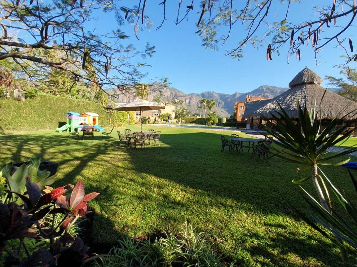 Un césped cuidado con muebles de exterior, una zona de juegos y una estructura con tejado de paja.