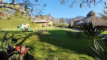 Un césped cuidado con muebles de exterior, una zona de juegos y una estructura con tejado de paja.