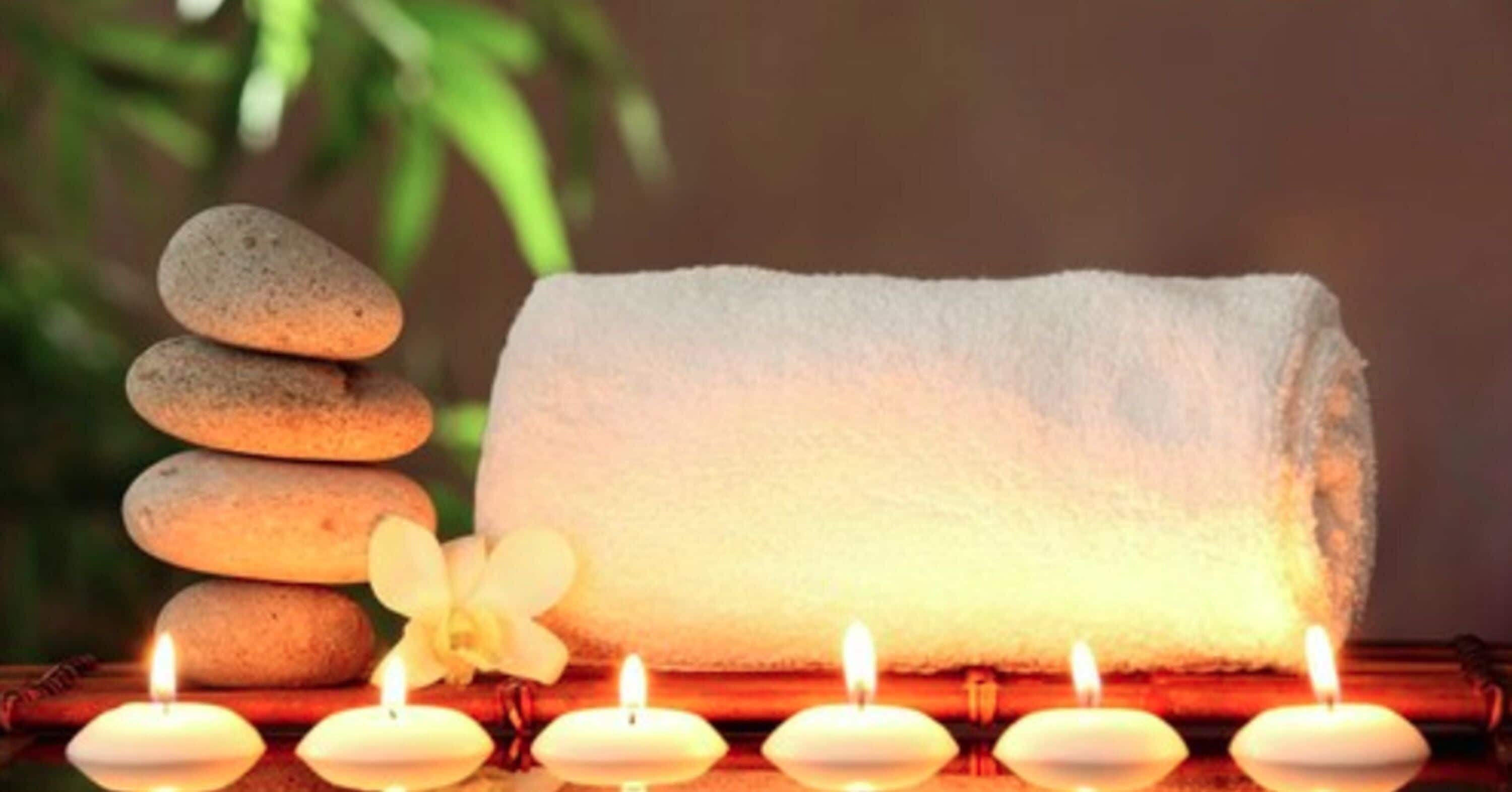 A stack of smooth stones, a white towel, and lit candles on a bamboo surface.