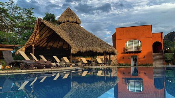A swimming pool with lounge chairs and a thatched-roof structure. - Hotel Real del Valle Tepoztlan (Tepoztlán)