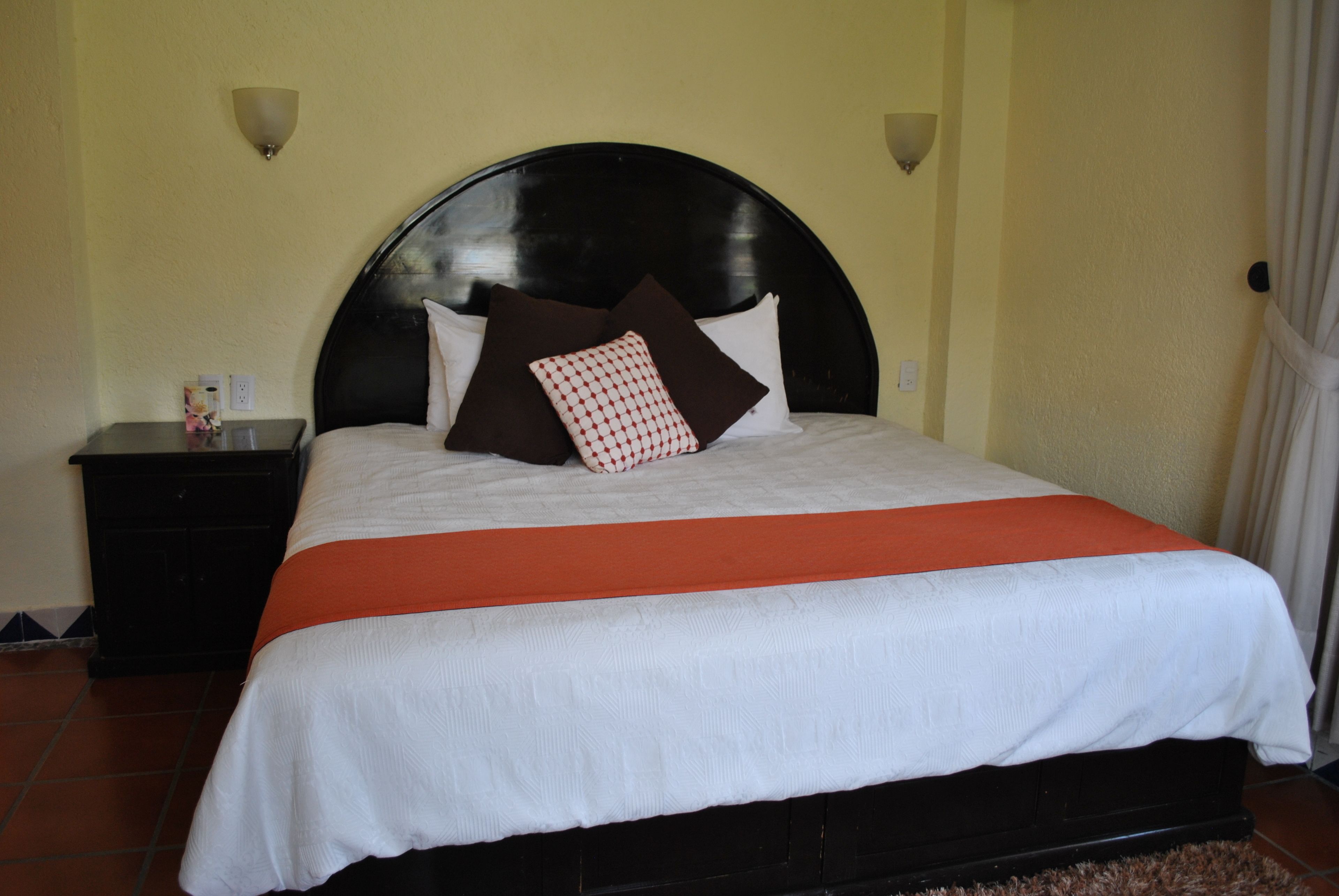 A bed with a black headboard, white bedding, and an orange accent.