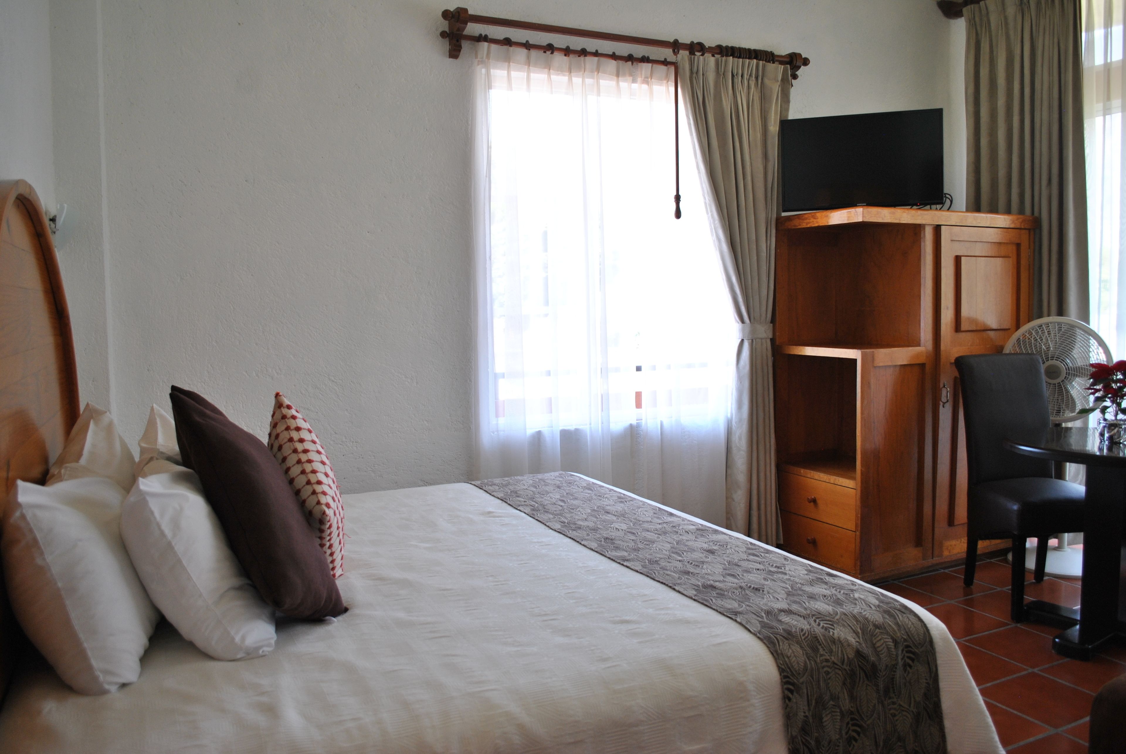 Une chambre d’hôtel avec un lit, un bureau, une chaise, une télévision et des rideaux.